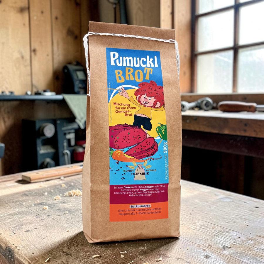 Papiertüte der Backmischung Pumuckl-Brot der Kunstmühle Hofmeir, 580 g, mit Pumuckl und rotem Gemüsebrot auf dem Etikett, auf einer Werkbank in Meister Eders Werkstatt