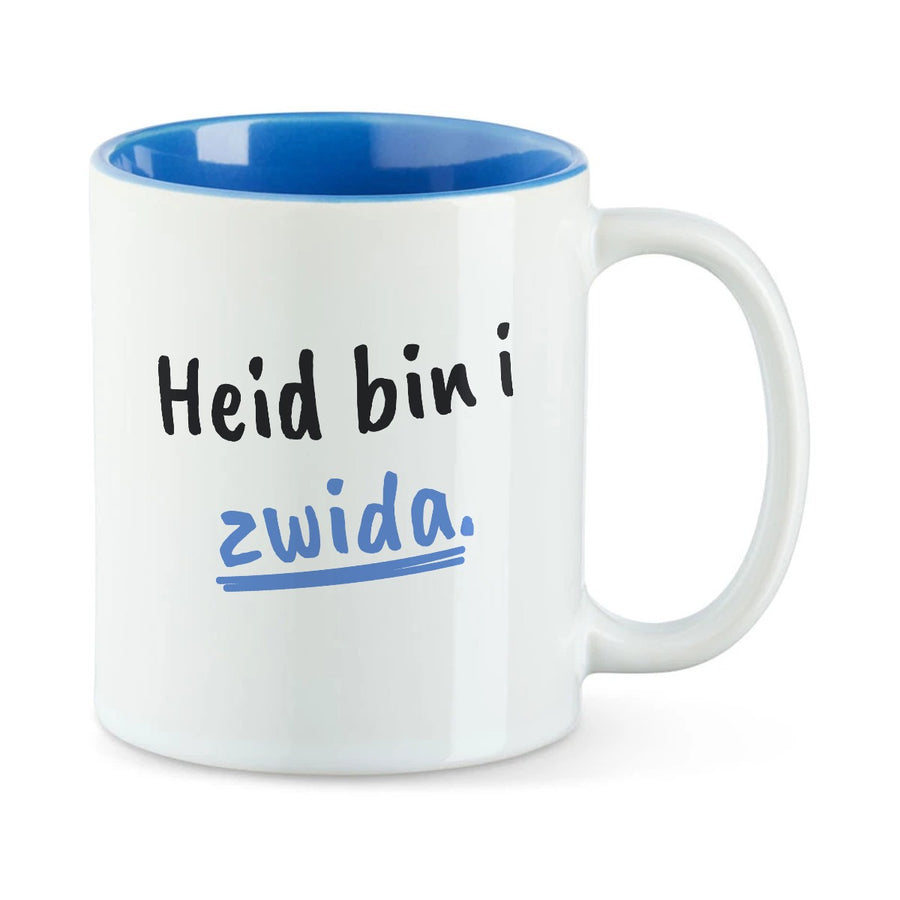 Weiße Tasse mit blauer Innenseite und dem bairischen Spruch „Heid bin i zwida.“ in Pinselschrift.