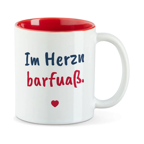Weiße Tasse mit roter Innenseite und dem bairischen Spruch „Im Herzn barfuaß.“ in Pinselschrift.