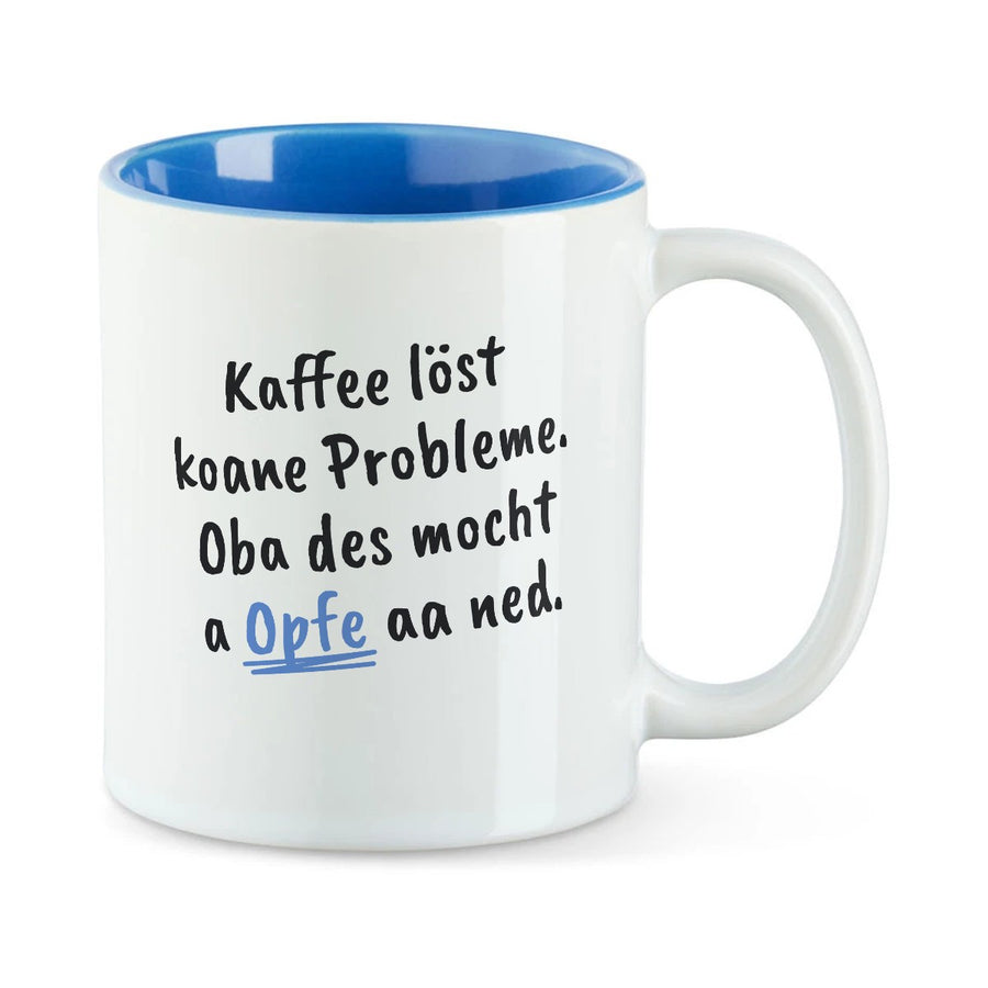 Weiße Tasse mit blauer Innenseite und dem bairischen Spruch „Kaffee löst koane Probleme. Oba des mocht a Opfe aa ned.“ in Pinselschrift.