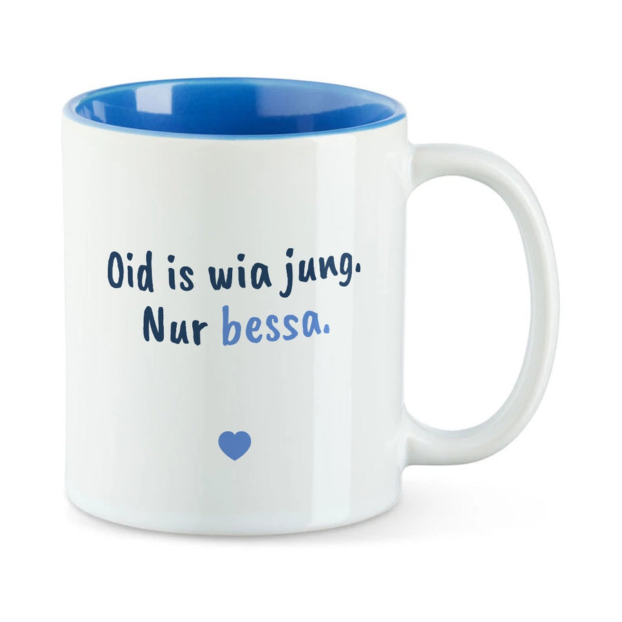 Weiße Tasse mit blauer Innenseite und dem bairischen Spruch „Oid is wia jung. Nur bessa.“ in Pinselschrift.