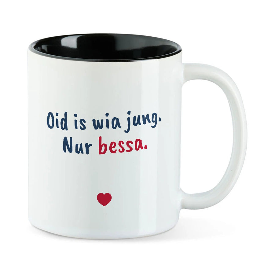 Weiße Tasse mit schwarzer Innenseite und dem bairischen Spruch „Oid is wia jung. Nur bessa.“ in Pinselschrift.