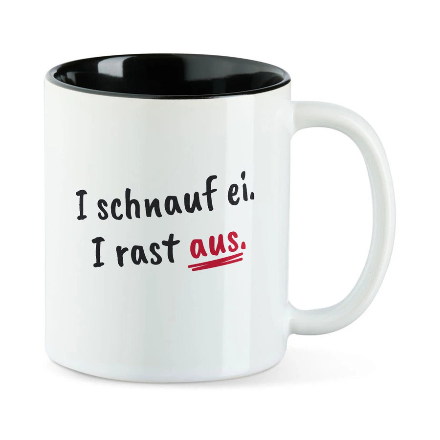 Weiße Tasse mit schwarzer Innenseite und dem bairischen Spruch „I schnauf ei. I rast aus.“ in Pinselschrift.