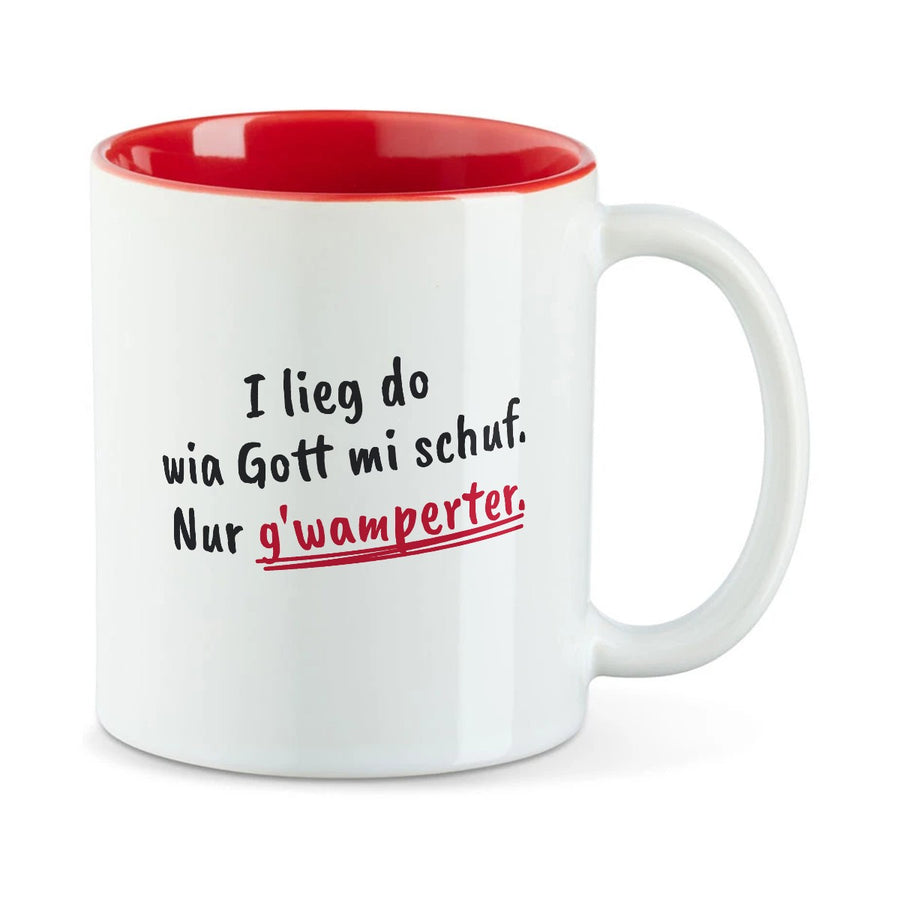 Weiße Tasse mit roter Innenseite und dem bairischen Spruch „I lieg do wia Gott mi schuf. Nur g'wamperter.“ in Pinselschrift.