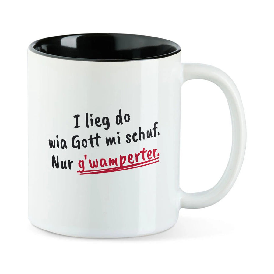 Weiße Tasse mit schwarzer Innenseite und dem bairischen Spruch „I lieg do wia Gott mi schuf. Nur g'wamperter.“ in Pinselschrift.
