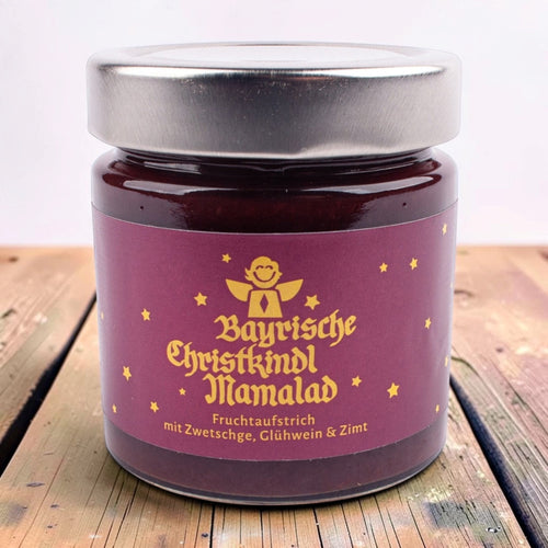 Glas Bayrische Christkindl Mamalad, Fruchtaufstrich mit Zwetschge, Glühwein und Zimt, lila Etikett mit goldenem Engel und Sternen, auf einem Holztisch.