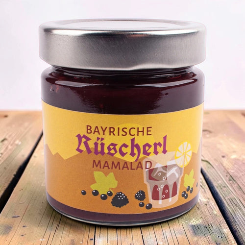 Glas Bayrische Rüscherl Mamalad, gelb-oranges Etikett mit Rüscherl-Glas und Beeren, auf einem Holztisch.