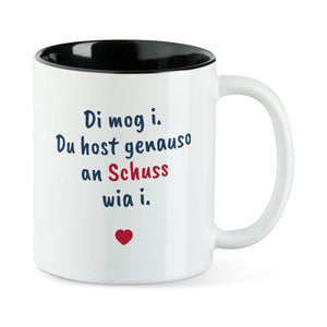 Weiße Tasse mit schwarzer Innenseite und dem bairischen Spruch „Di mog i. Du host genauso an Schuss wia i.“ in Pinselschrift.