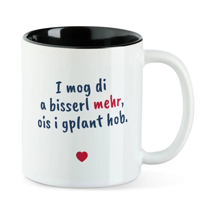Weiße Tasse mit schwarzer Innenseite und dem bairischen Spruch „I mog di a bisserl mehr, ois i gplant hob.“ in Pinselschrift.