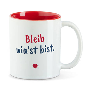 Weiße Tasse mit roter Innenseite und dem bairischen Spruch „Bleib wia'st bist.“ in Pinselschrift.