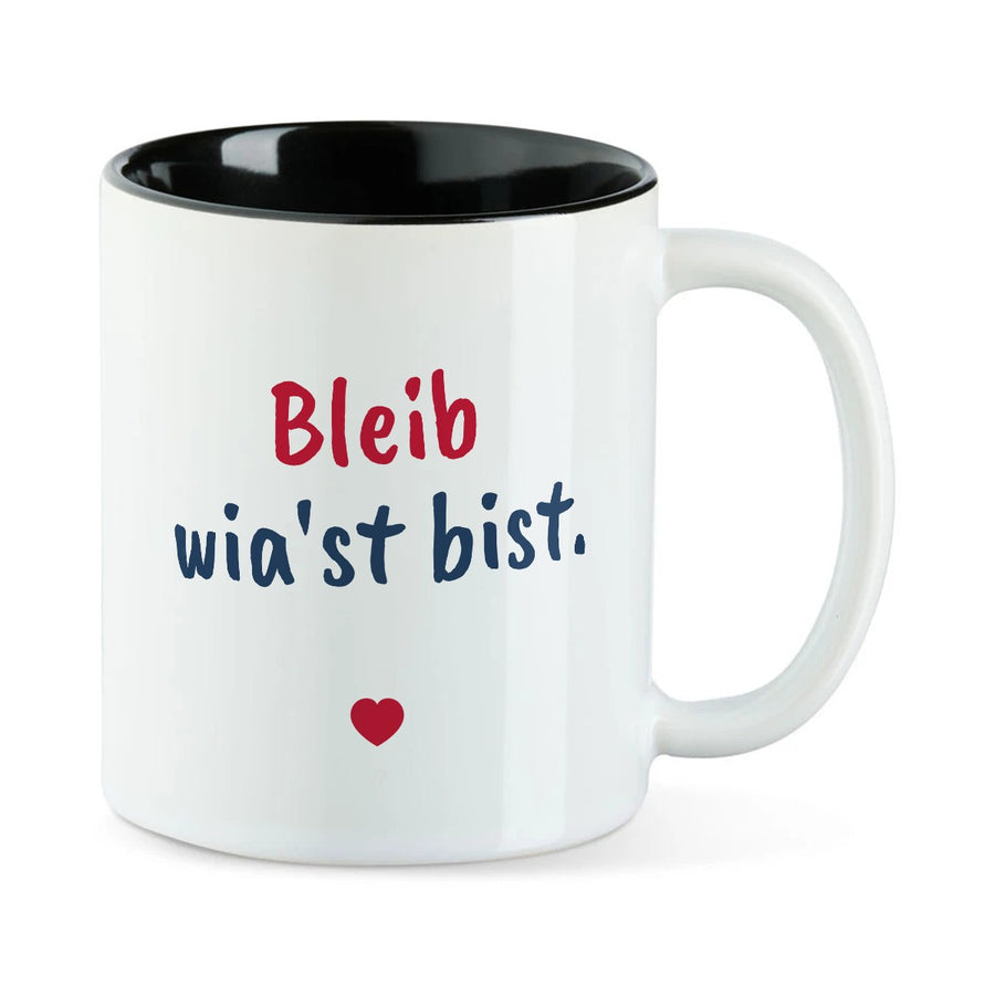 Weiße Tasse mit schwarzer Innenseite und dem bairischen Spruch „Bleib wia'st bist.“ in Pinselschrift.