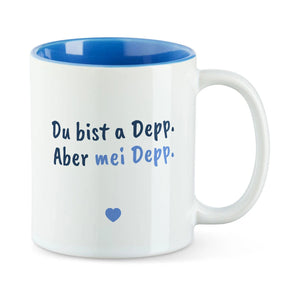 Weiße Tasse mit blauer Innenseite und dem bairischen Spruch „Du bist a Depp. Aber mei Depp.“ in Pinselschrift.