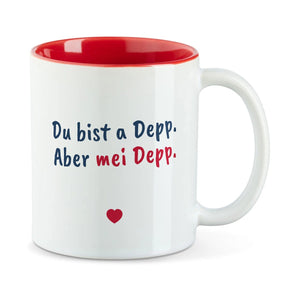 Weiße Tasse mit roter Innenseite und dem bairischen Spruch „Du bist a Depp. Aber mei Depp.“ in Pinselschrift.