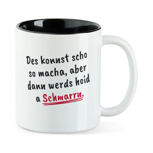 Weiße Tasse mit schwarzer Innenseite und dem bairischen Spruch „Des konnst scho so macha, aber dann werds hoid a Schmarrn.“ in Pinselschrift.