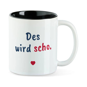 Weiße Tasse mit schwarzer Innenseite und dem bairischen Spruch „Des wird scho.“ in Pinselschrift.