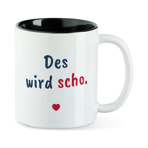 Weiße Tasse mit schwarzer Innenseite und dem bairischen Spruch „Des wird scho.“ in Pinselschrift.