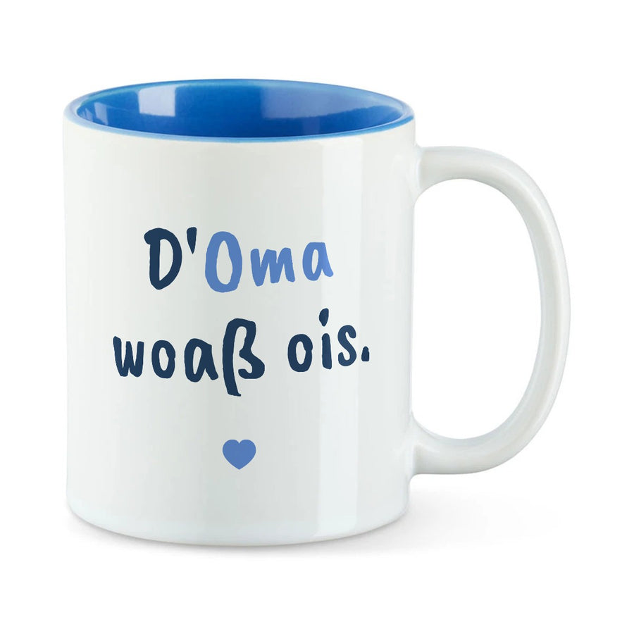 Weiße Tasse mit blauer Innenseite und dem bairischen Spruch „D'Oma woaß ois.“ in Pinselschrift.