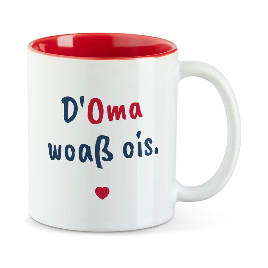 Weiße Tasse mit roter Innenseite und dem bairischen Spruch „D'Oma woaß ois.“ in Pinselschrift.