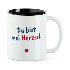 Weiße Tasse mit schwarzer Innenseite und dem bairischen Spruch „Du bist mei Herzerl.“ in Pinselschrift.