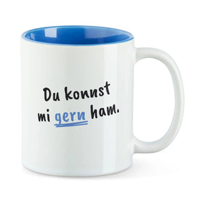 Weiße Tasse mit blauer Innenseite und dem bairischen Spruch „Du konnst mi gern ham.“ in Pinselschrift.