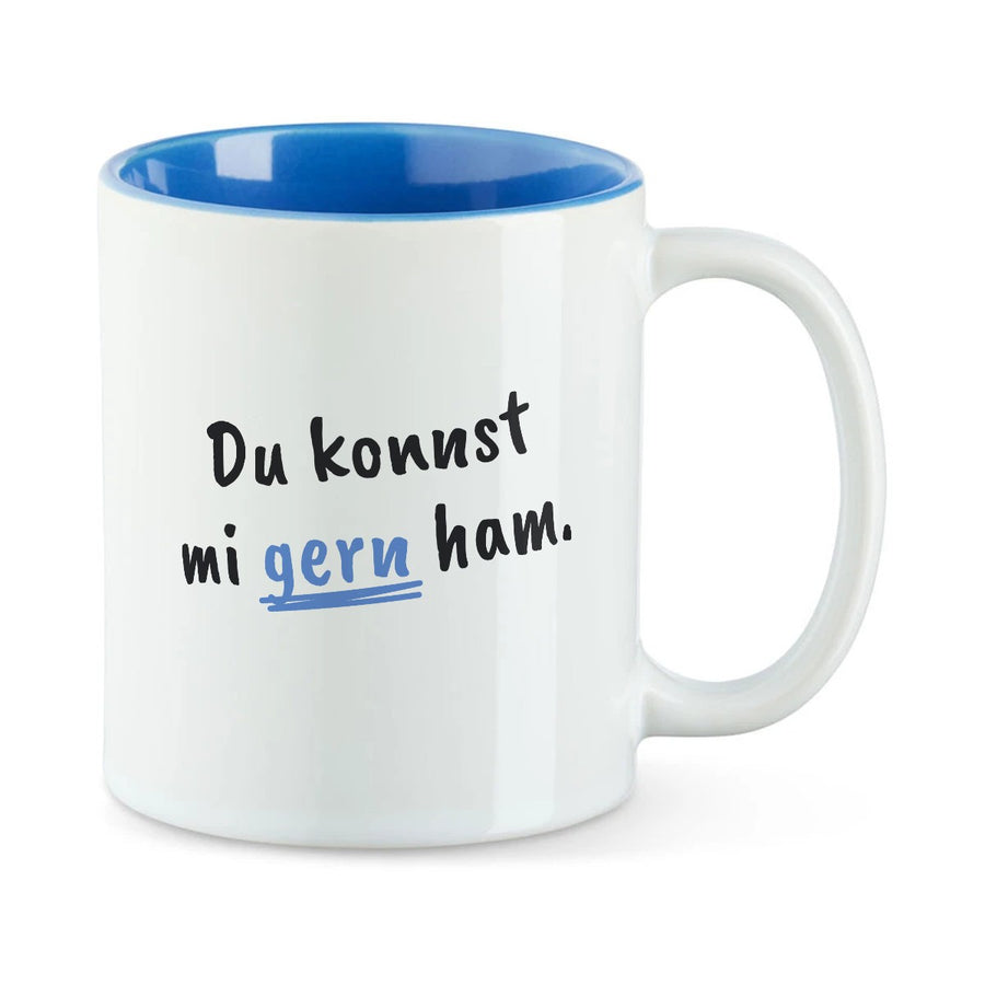 Weiße Tasse mit blauer Innenseite und dem bairischen Spruch „Du konnst mi gern ham.“ in Pinselschrift.