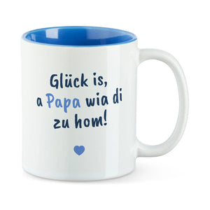 Weiße Tasse mit blauer Innenseite und dem bairischen Spruch „Glück is, a Papa wia di zu hom!“ in Pinselschrift.
