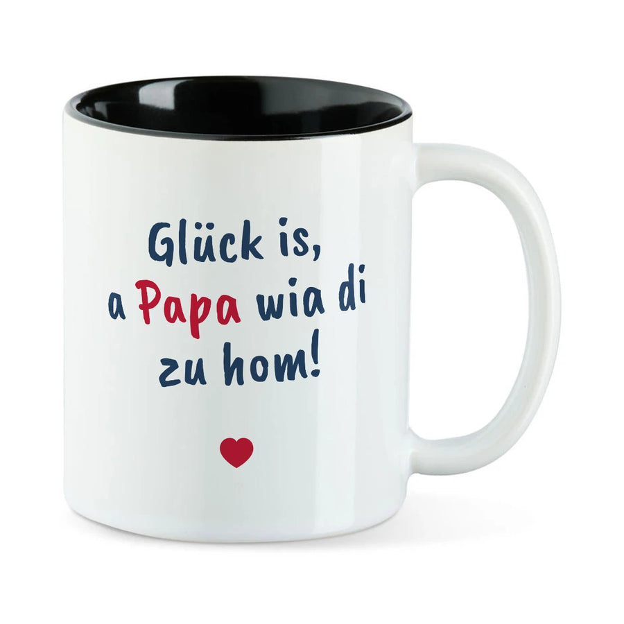 Weiße Tasse mit schwarzer Innenseite und dem bairischen Spruch „Glück is, a Papa wia di zu hom!“ in Pinselschrift.