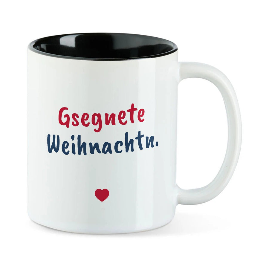 Weiße Tasse mit schwarzer Innenseite und dem bairischen Spruch „Gsegnete Weihnachtn.“ in Pinselschrift.