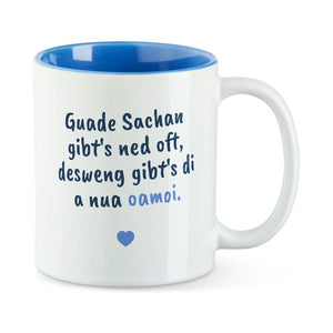 Weiße Tasse mit blauer Innenseite und dem bairischen Spruch „Guade Sachan gibt's ned oft, desweng gibt's di a nua oamoi.“ in Pinselschrift.