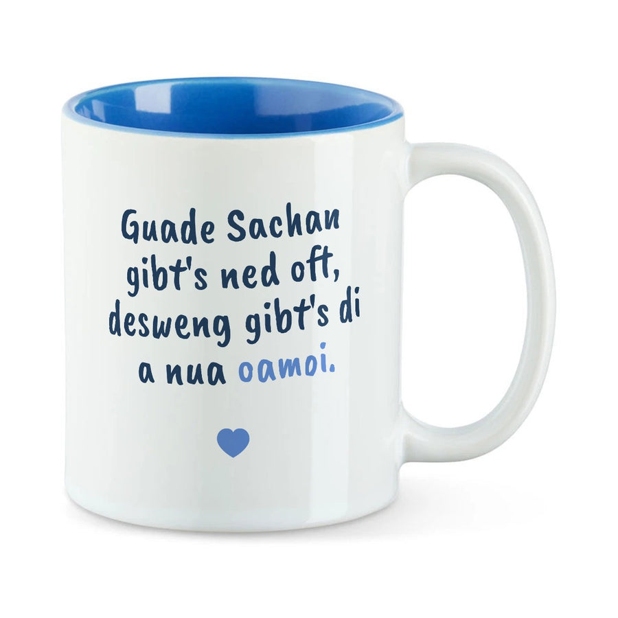 Weiße Tasse mit blauer Innenseite und dem bairischen Spruch „Guade Sachan gibt's ned oft, desweng gibt's di a nua oamoi.“ in Pinselschrift.
