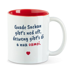 Weiße Tasse mit roter Innenseite und dem bairischen Spruch „Guade Sachan gibt's ned oft, desweng gibt's di a nua oamoi.“ in Pinselschrift.