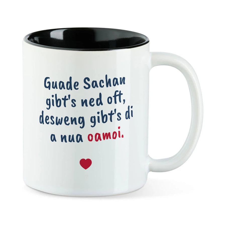 Weiße Tasse mit schwarzer Innenseite und dem bairischen Spruch „Guade Sachan gibt's ned oft, desweng gibt's di a nua oamoi.“ in Pinselschrift.