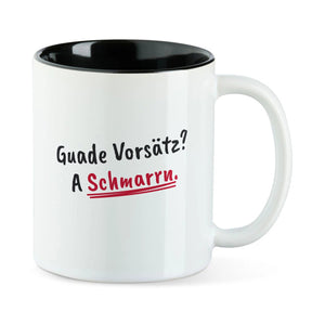 Weiße Tasse mit schwarzer Innenseite und dem bairischen Spruch „Guade Vorsätz? A Schmarrn.“ in Pinselschrift.