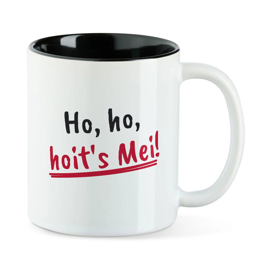 Weiße Tasse mit schwarzer Innenseite und dem bairischen Spruch „Ho, ho, hoit's Mei!“ in Pinselschrift.