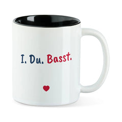 Weiße Tasse mit schwarzer Innenseite und dem bairischen Spruch „I. Du. Basst.“ in Pinselschrift.