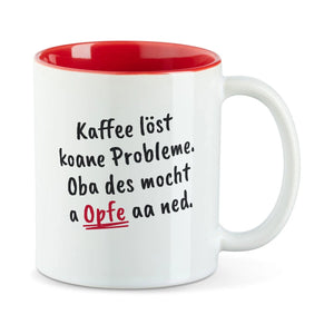 Weiße Tasse mit roter Innenseite und dem bairischen Spruch „Kaffee löst koane Probleme. Oba des mocht a Opfe aa ned.“ in Pinselschrift.