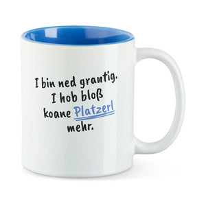 Weiße Tasse mit blauer Innenseite und dem bairischen Spruch „I bin ned grantig. I hob bloß koane Platzerl mehr.“ in Pinselschrift.