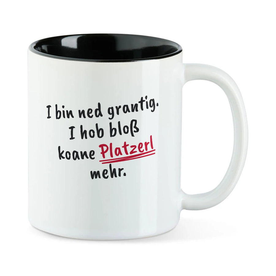 Weiße Tasse mit schwarzer Innenseite und dem bairischen Spruch „I bin ned grantig. I hob bloß koane Platzerl mehr.“ in Pinselschrift.