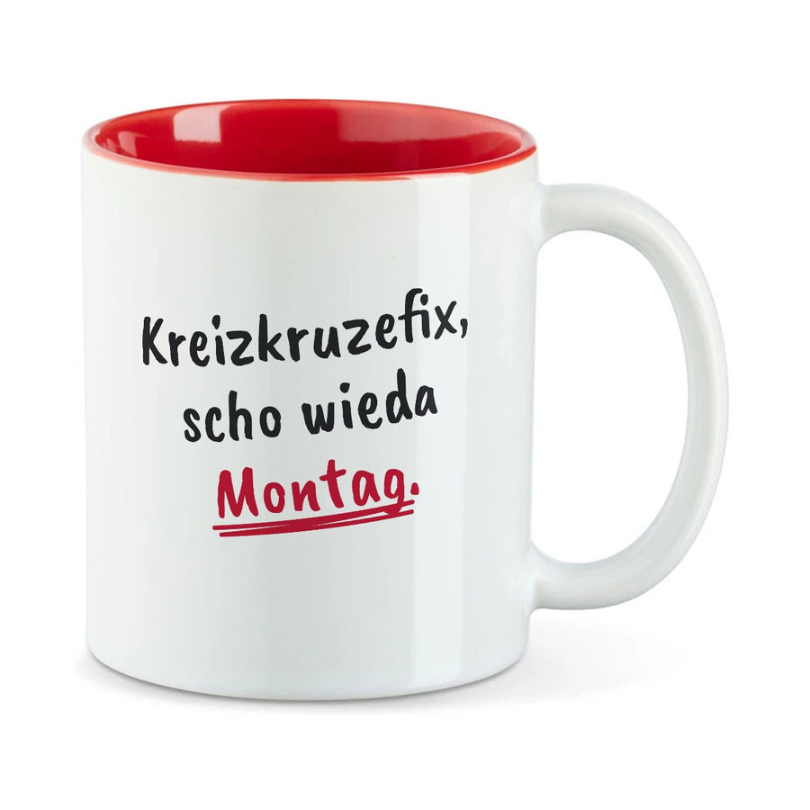 Weiße Tasse mit roter Innenseite und dem bairischen Spruch „Kreizkruzefix, scho wieda Montag.“ in Pinselschrift.