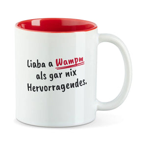 Weiße Tasse mit roter Innenseite und dem bairischen Spruch „Liaba a Wampm als gar nix Hervorragendes.“ in Pinselschrift.