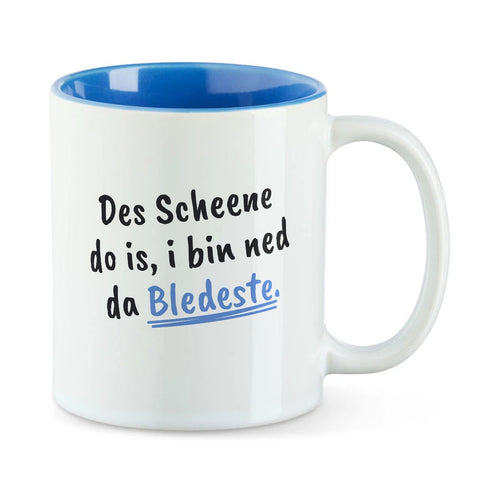 Weiße Tasse mit blauer Innenseite und dem bairischen Spruch „Des Scheene do is, i bin ned da Bledeste.“ in Pinselschrift.