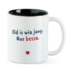 Weiße Tasse mit schwarzer Innenseite und dem bairischen Spruch „Oid is wia jung. Nur bessa.“ in Pinselschrift.