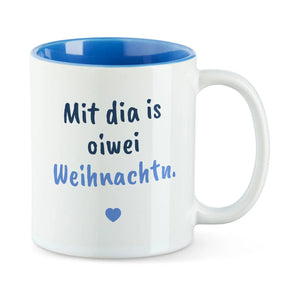 Weiße Tasse mit blauer Innenseite und dem bairischen Spruch „Mit dia is oiwei Weihnachtn.“ in Pinselschrift.