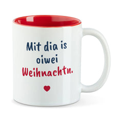 Weiße Tasse mit roter Innenseite und dem bairischen Spruch „Mit dia is oiwei Weihnachtn.“ in Pinselschrift.