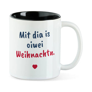 Weiße Tasse mit schwarzer Innenseite und dem bairischen Spruch „Mit dia is oiwei Weihnachtn.“ in Pinselschrift.