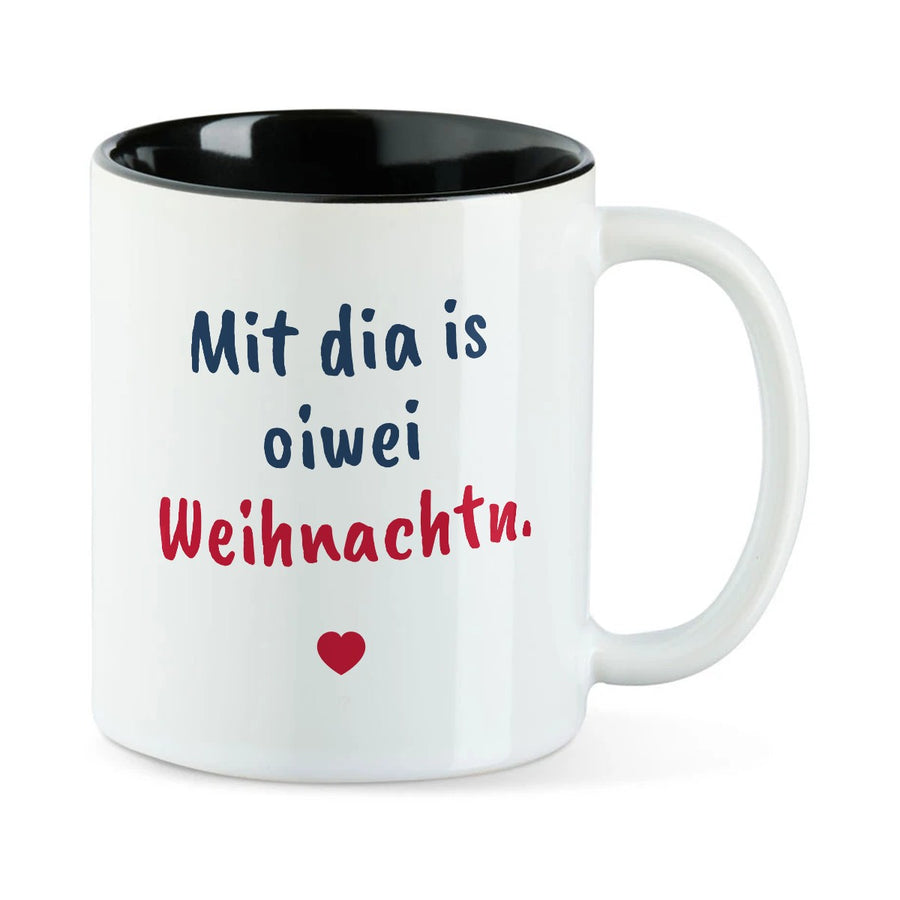 Weiße Tasse mit schwarzer Innenseite und dem bairischen Spruch „Mit dia is oiwei Weihnachtn.“ in Pinselschrift.