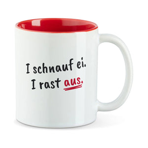 Weiße Tasse mit roter Innenseite und dem bairischen Spruch „I schnauf ei. I rast aus.“ in Pinselschrift.