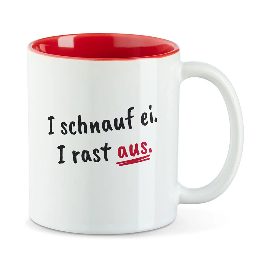 Weiße Tasse mit roter Innenseite und dem bairischen Spruch „I schnauf ei. I rast aus.“ in Pinselschrift.