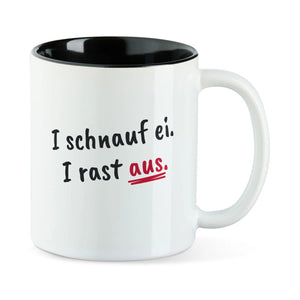 Weiße Tasse mit schwarzer Innenseite und dem bairischen Spruch „I schnauf ei. I rast aus.“ in Pinselschrift.