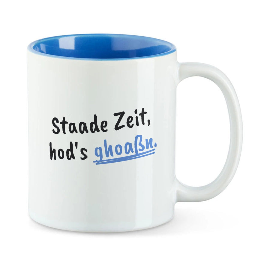 Weiße Tasse mit blauer Innenseite und dem bairischen Spruch „Staade Zeit, hod's ghoaßn.“ in Pinselschrift.